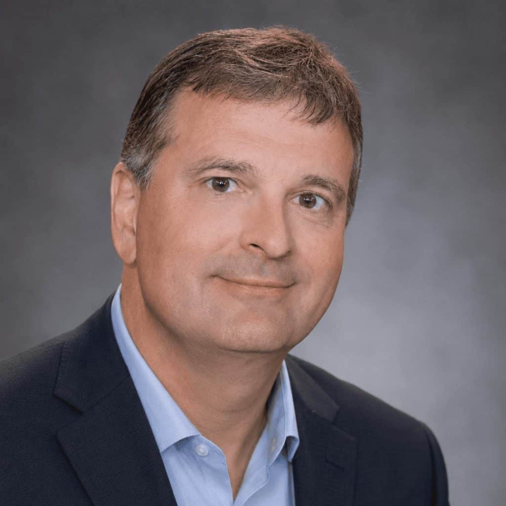 Portrait of a middle-aged man wearing a dark suit jacket and light blue collared shirt.